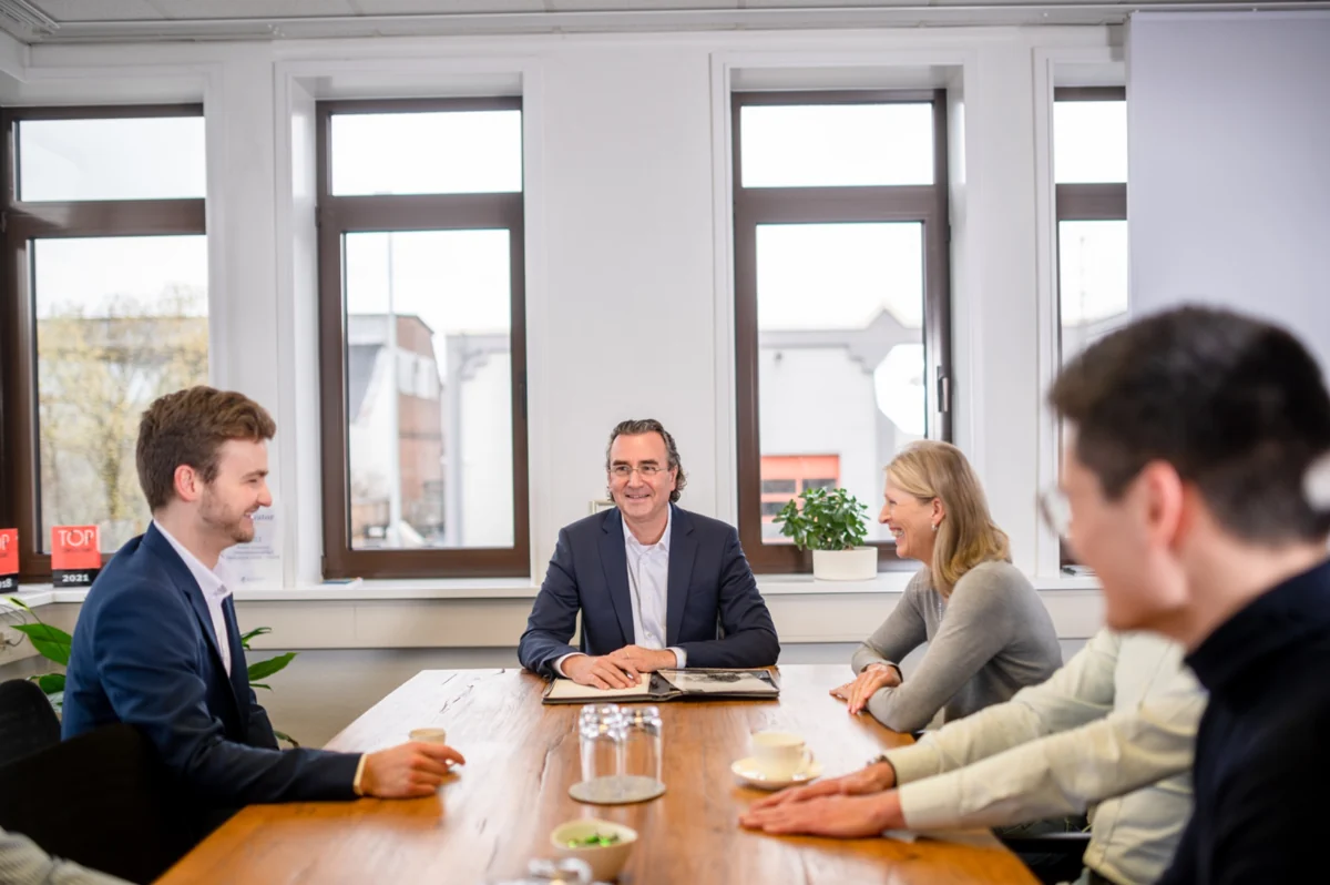 ROland Schwarzer mit drei Gesprächspartnern an einem Tisch in einem hellen Besprechungsraum
